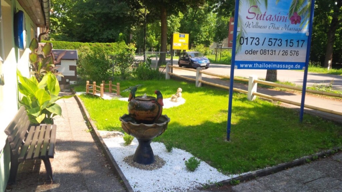 Außenbereich mit Brunnen, Bank und Firmenschild von Sutasini Wellness Thai Massage
