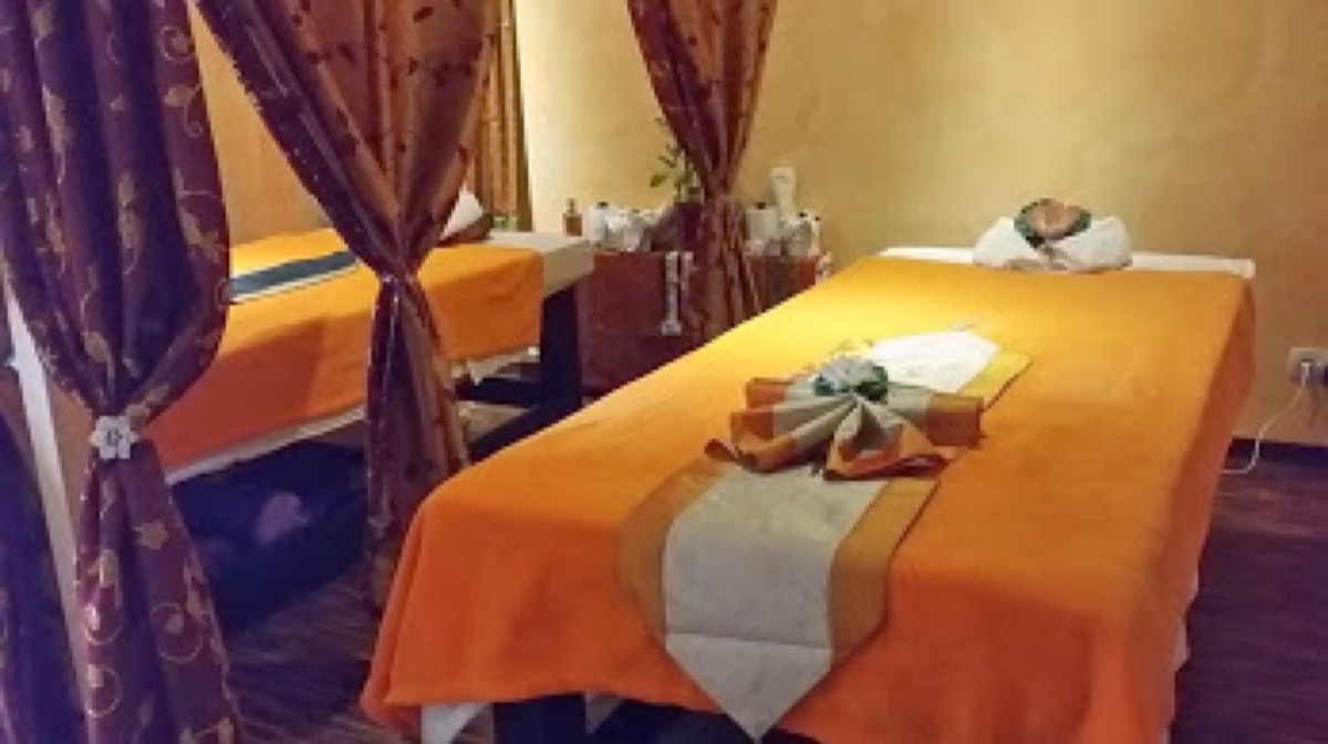 Zwei Massageliegen mit orangefarbenen Tüchern hinter Vorhängen im Studio
