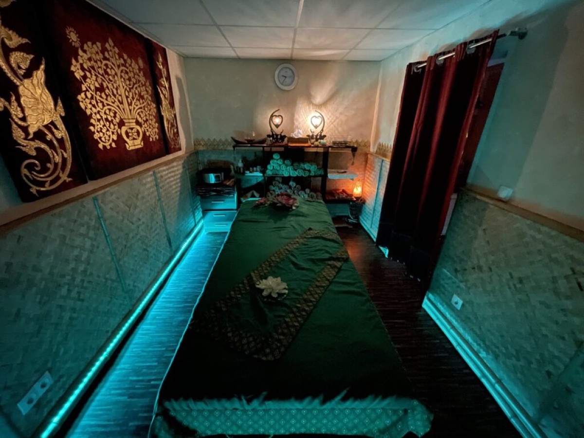 Behandlungsraum mit grüner Massageliege, goldener Thai-Wandkunst und warmem Licht